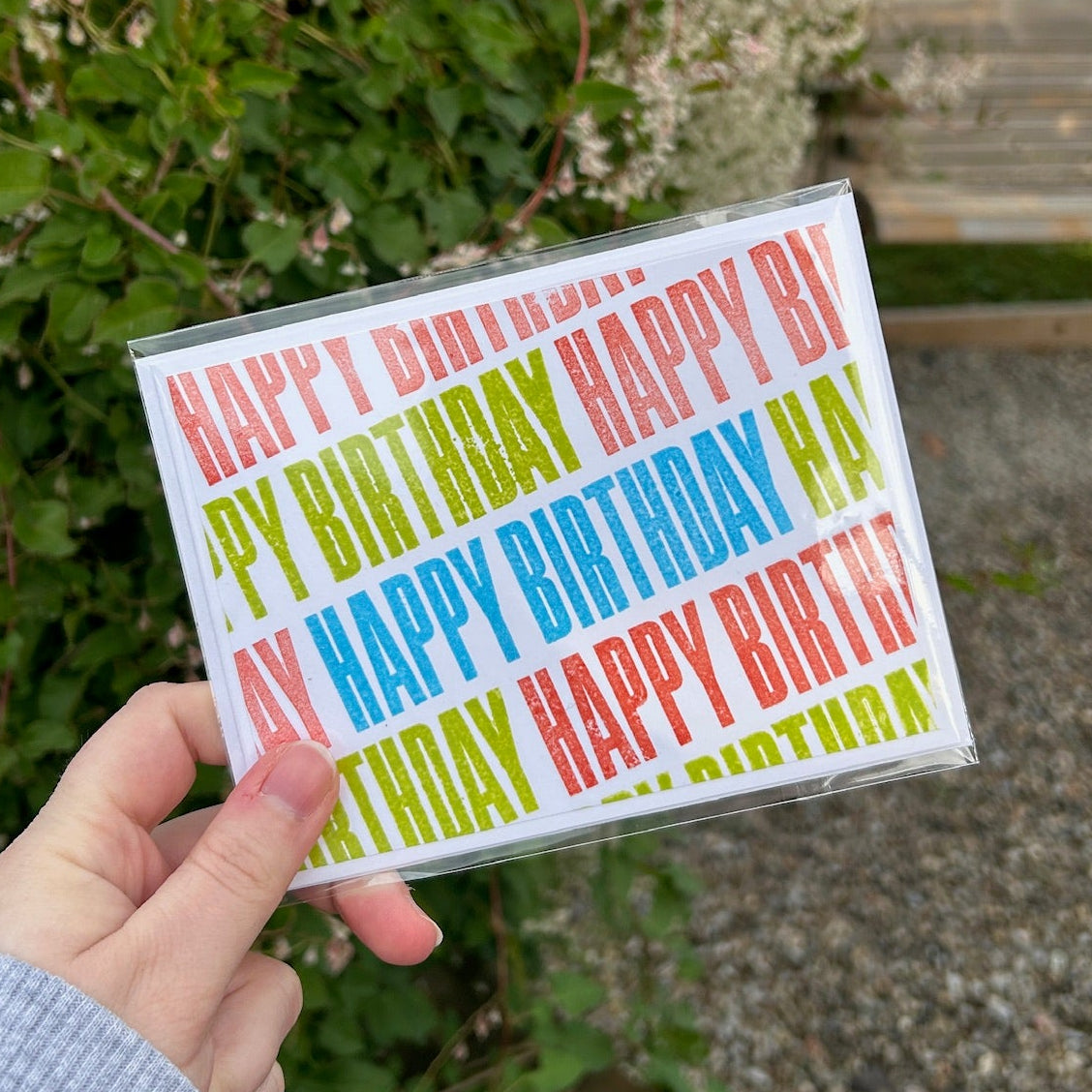 A colourful 'Happy Birthday' card in front of a garden background
