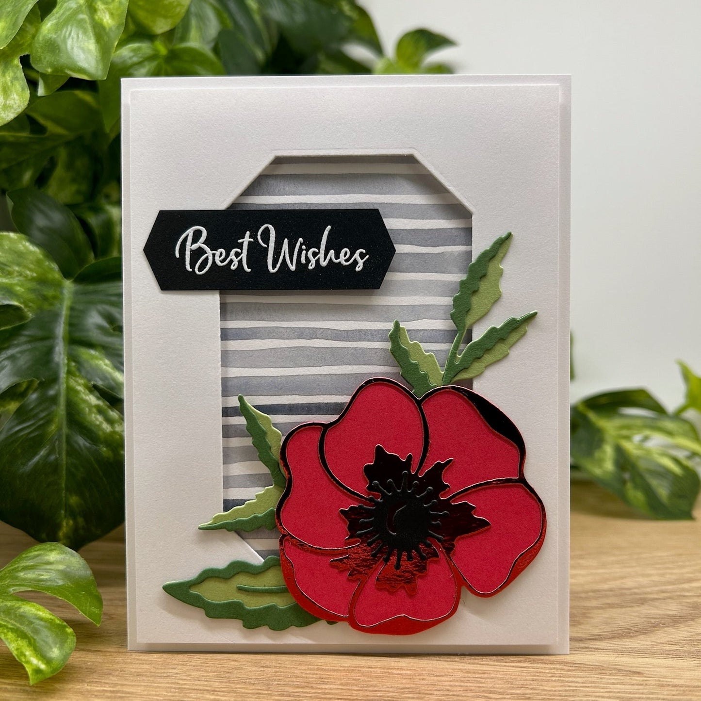 Card with a red flower design and 'Best Wishes' text, set against a green leafy background.