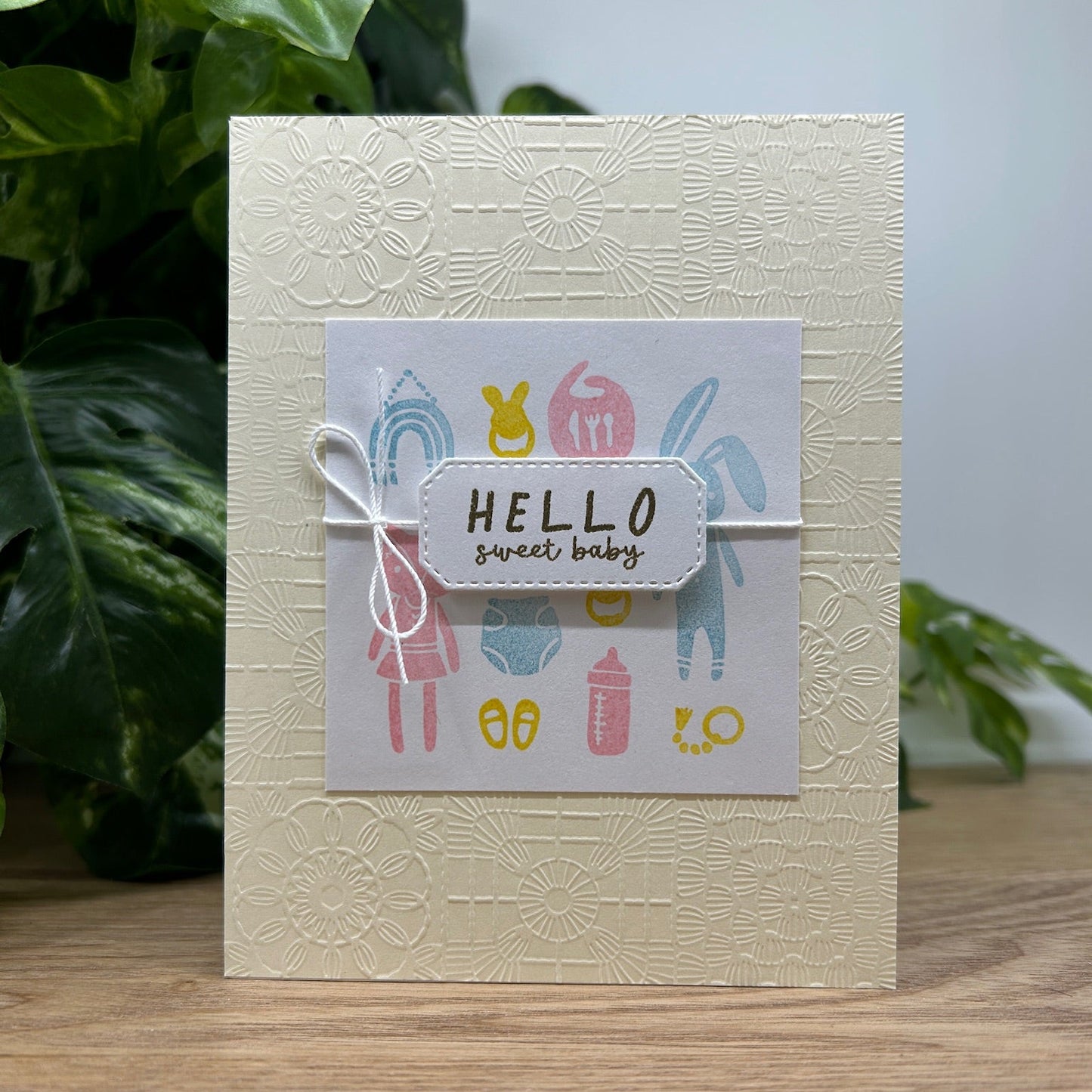 Greeting card with 'Hello sweet baby' text and baby-themed illustrations on a textured beige background.